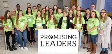 Students stand in the Science Center with a banner that reads "Promising Leaders"