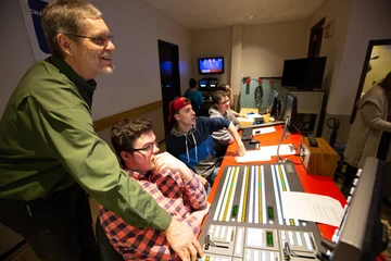 a professor assists a student operating the television switcher in the tv studio